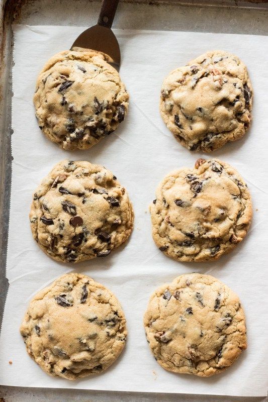 six chocolate chip cookies sitting on top of a baking sheet next to a spatula