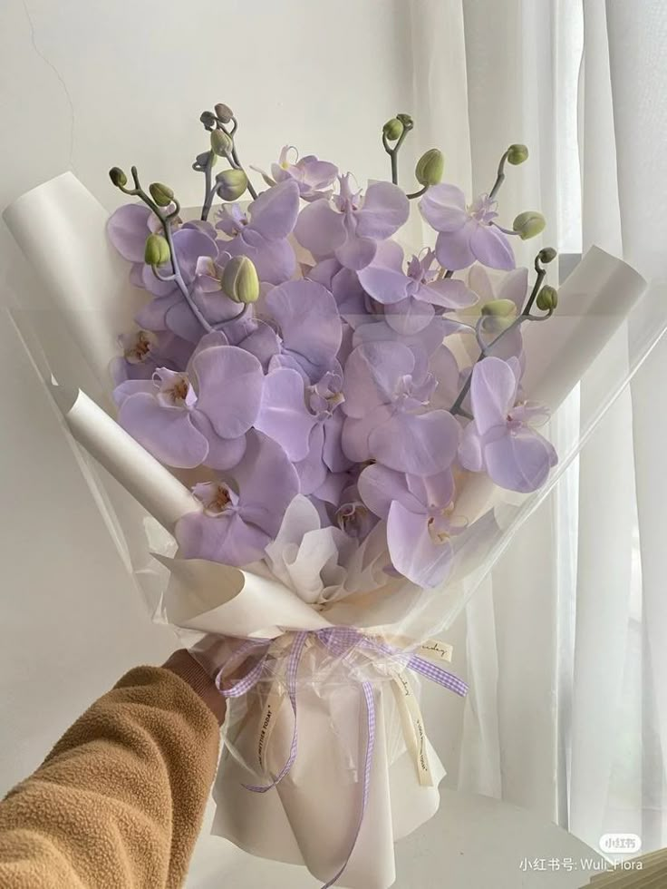 a bouquet of purple flowers is being held by a person's hand in front of a window