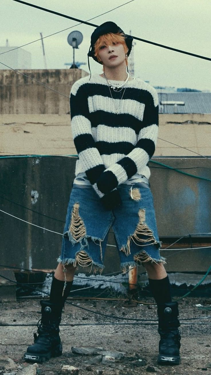 a young man wearing ripped jeans and a black and white striped sweater standing in front of a building