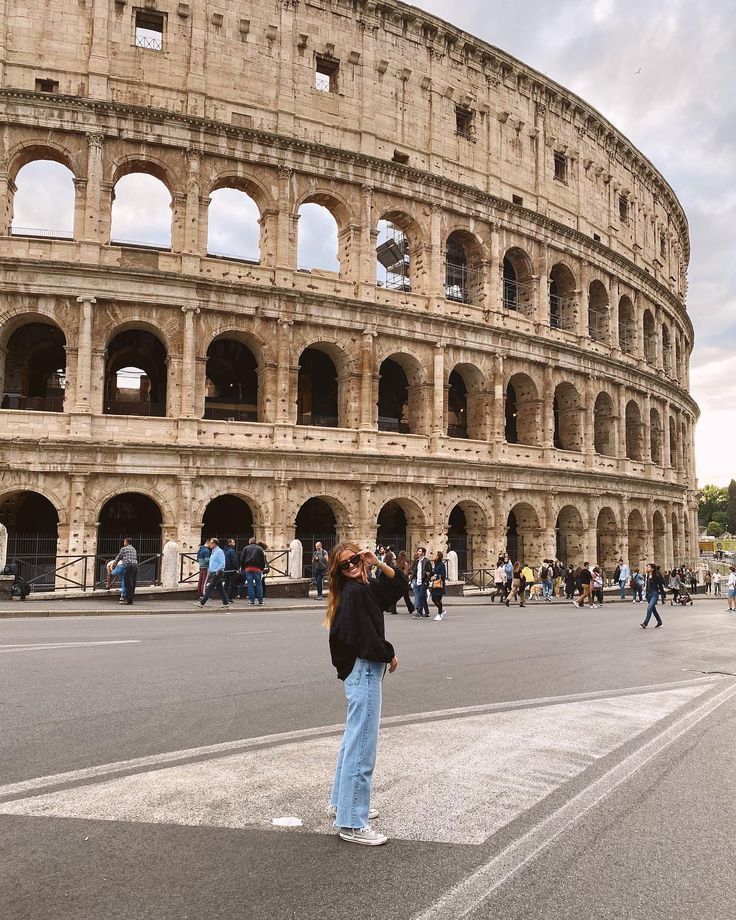 a woman standing in front of the colossion looking up at her cell phone