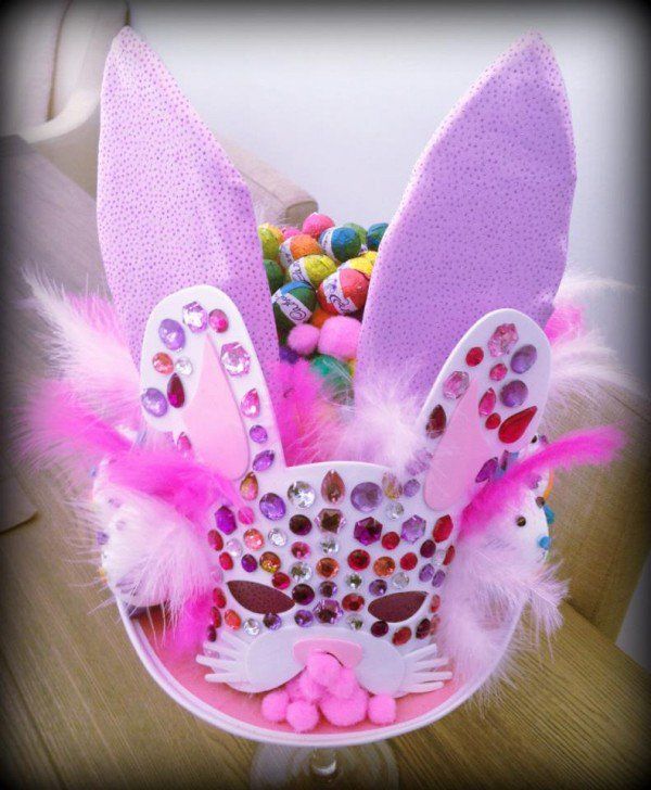 an easter bunny mask with pink feathers and jewels on it's ears, sitting on a table