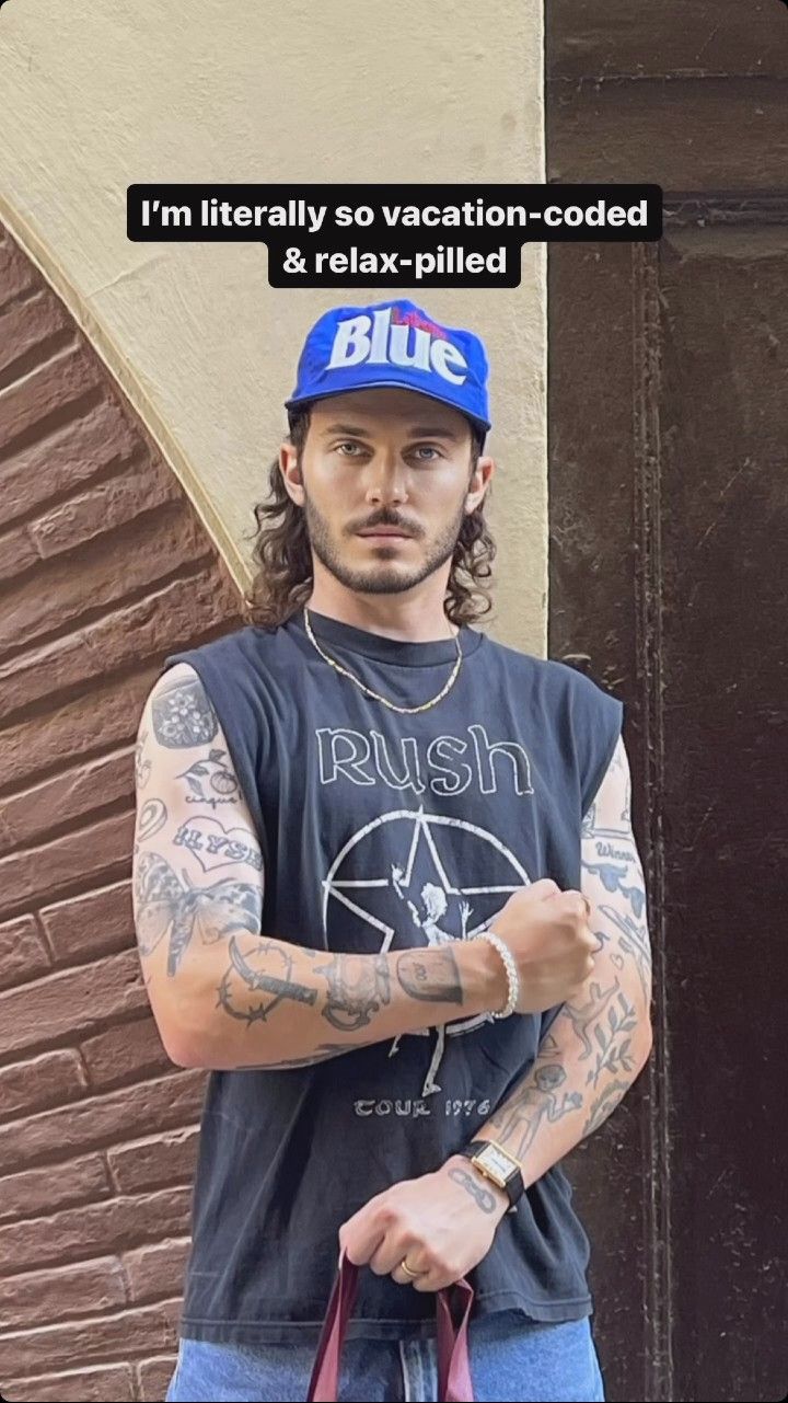 a man with long hair and tattoos holding a bag