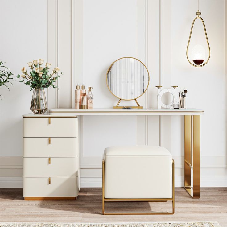 a white dressing table with gold accents and flowers in vases next to the mirror