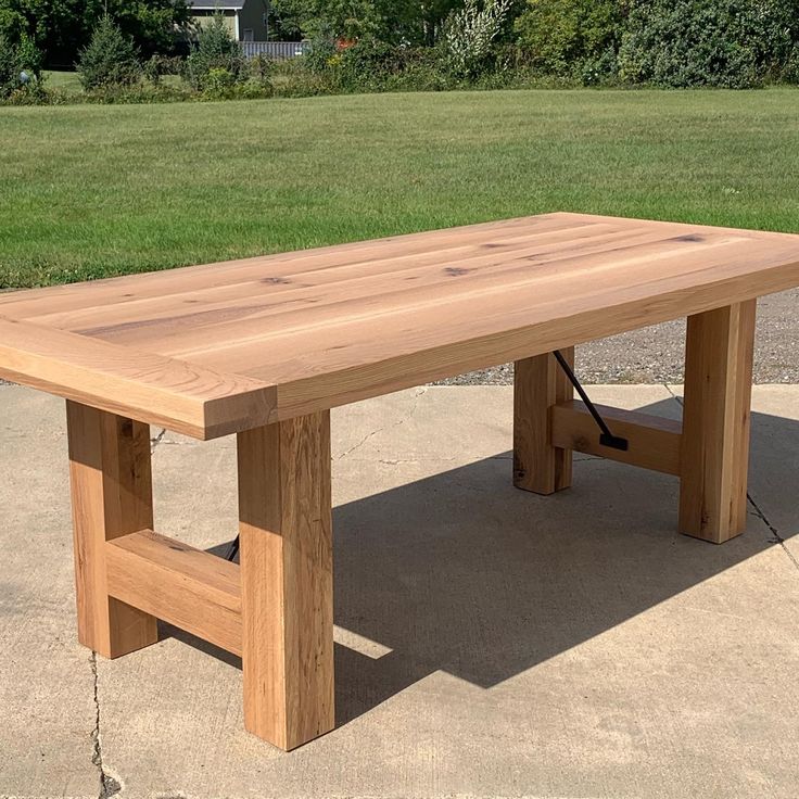 a wooden table sitting on top of a cement ground next to a field and trees