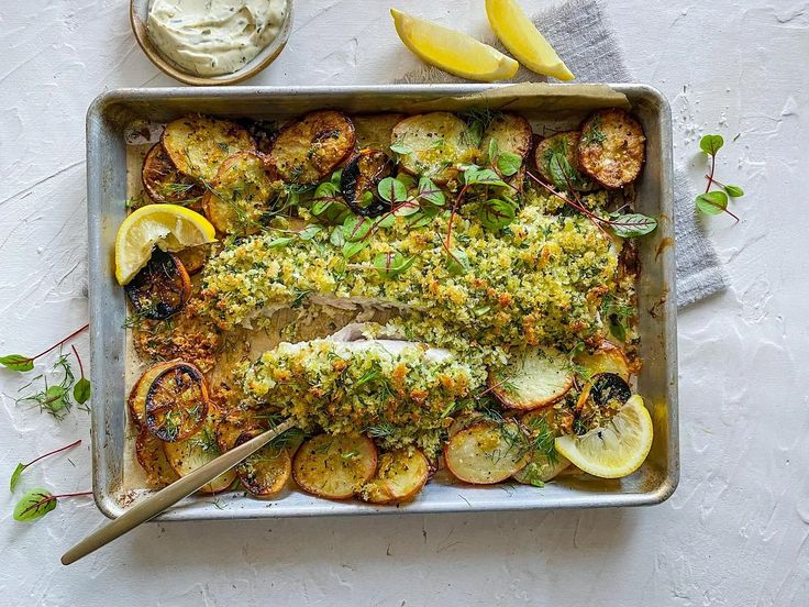 a pan filled with fish covered in herbs next to lemon wedges and some sauce