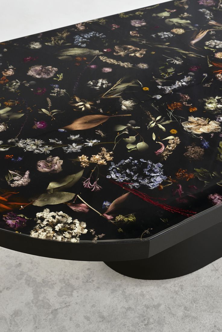 a black table topped with lots of flowers on top of a white floor next to a wall