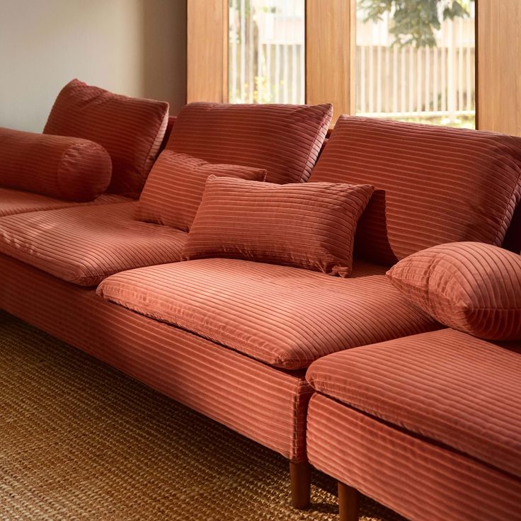 a red couch sitting in front of a window with pillows on top of the couch