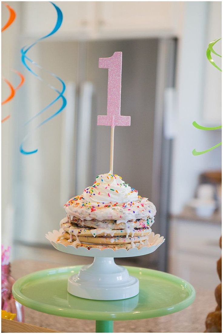 a birthday cake with sprinkles and a one candle on top is sitting on a green plate