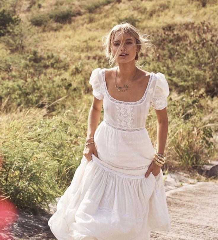 a woman in a white dress is walking down the road with her hands on her hips