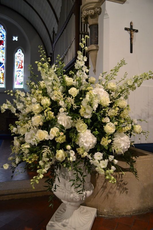 a vase filled with white flowers sitting on top of a wooden floor next to a cross