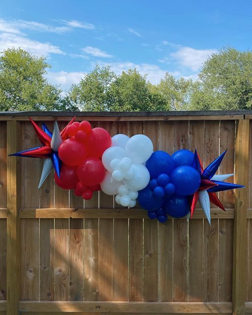 balloons in the shape of stars are attached to a wooden fence with red, white and blue balloons