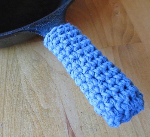 a blue crocheted dish cloth sitting on top of a wooden table next to a skillet