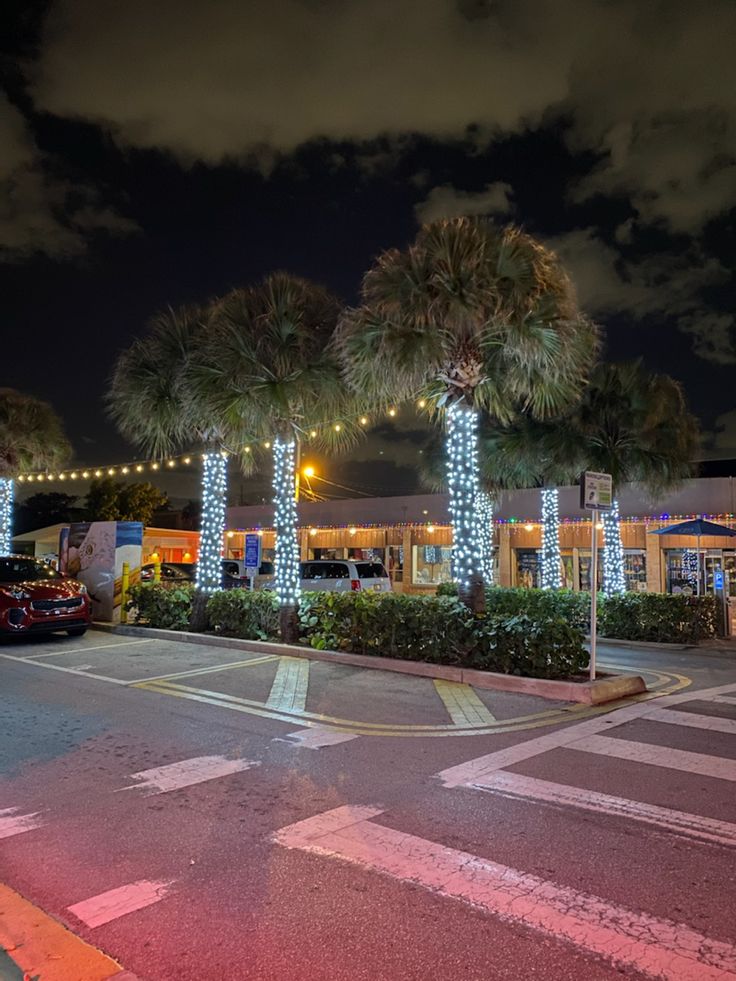 palm trees are lit up in front of a shopping center with cars parked on the street