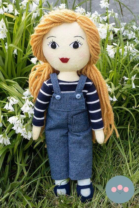 a doll with blonde hair and blue overalls stands in front of white daisies