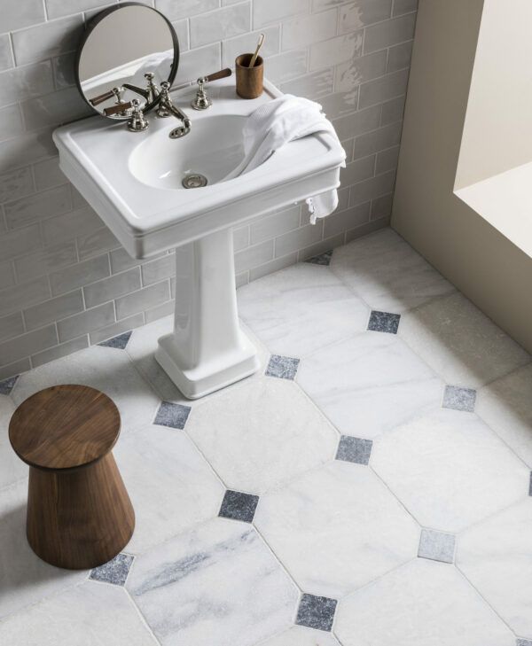 a white sink sitting next to a wooden stool in a bathroom under a large mirror