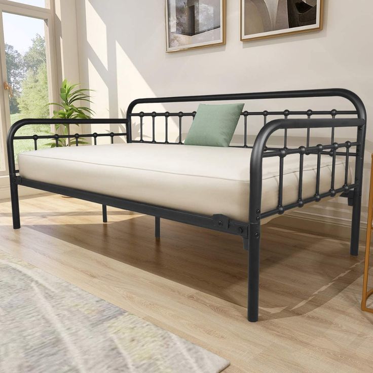 a black metal daybed sitting on top of a hard wood floor next to a window