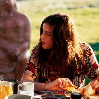 a woman sitting at a table with food in front of her and a statue behind her