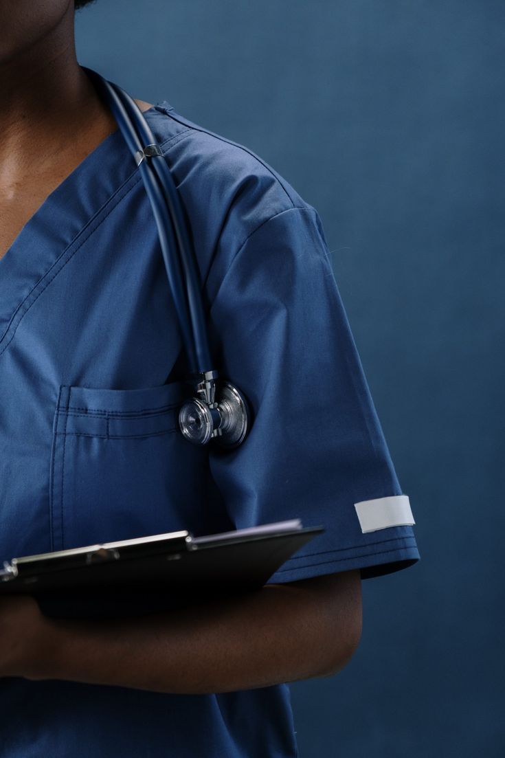 a woman in scrubs holding a clipboard and wearing a stethoscope