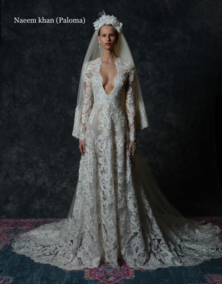 a woman wearing a wedding dress with long sleeves and a veil on her head is standing in front of a dark background