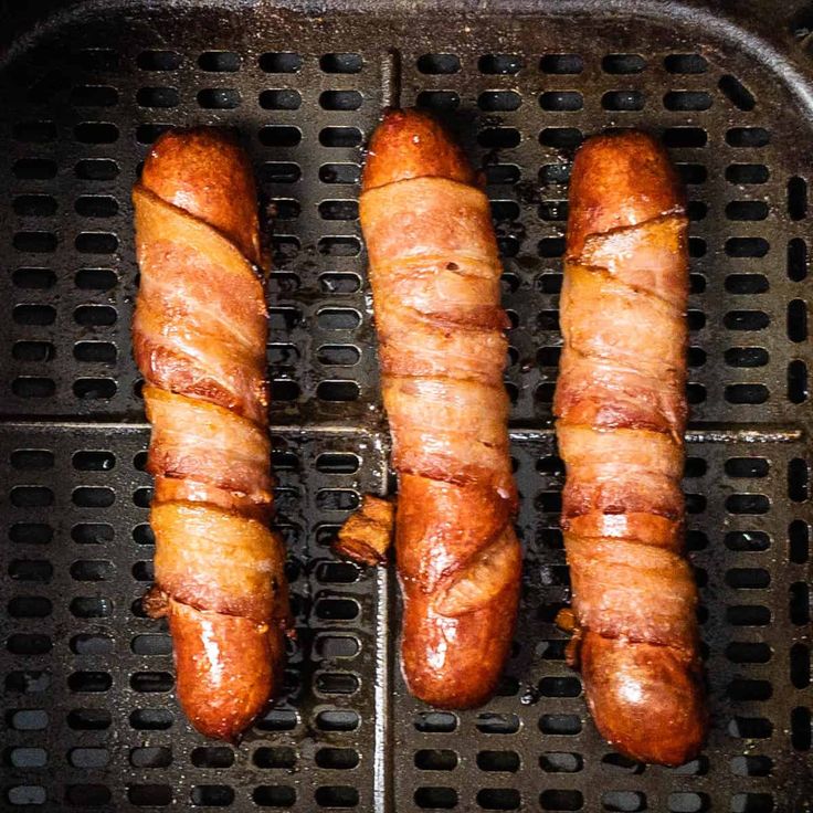 three sausages being cooked on a grill with one wrapped in bacon and the other uncooked