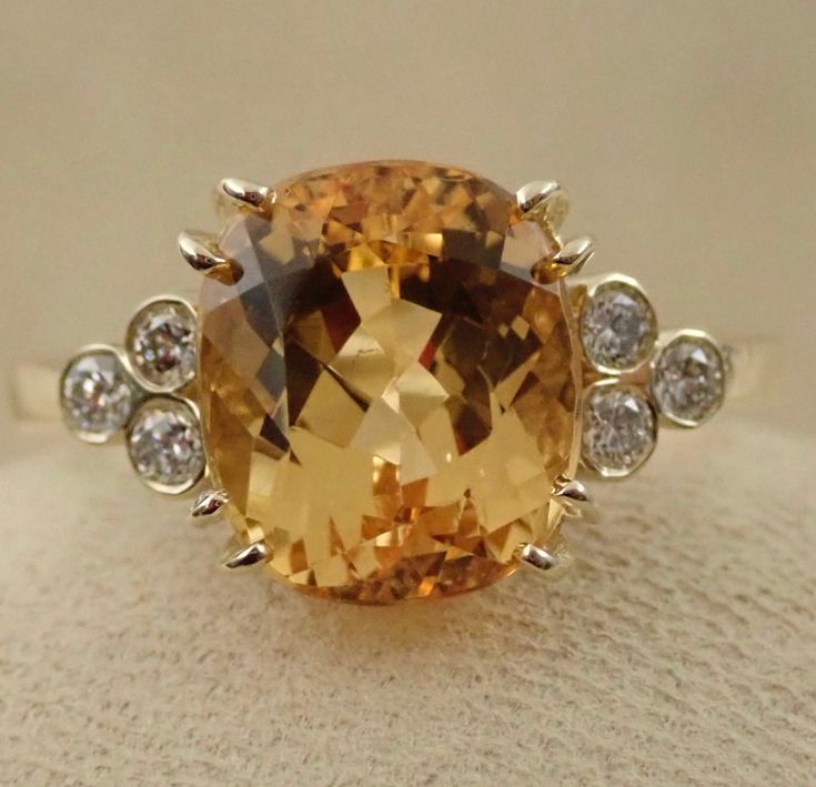 "This beautiful engagement ring is made in 14k yellow gold. The natural imperial topaz weight is 4.35 carats. The 6 bezel set side diamonds are VS clarity and G color range .18 carats total weight . Total gem weight 4.53 carats. We can make it any size from 5-7 and you still be able to return it within the listed time frame. Sizing outside of that range requires a resize fee if for any reason the ring is retuned. Ring sizing may add additional handling time. We love this ring because it represen Imperial Topaz Engagement Ring, Yellow Topaz Ring, Engagement Ring Cushion, Huge Rings, Ring Cushion, Citrine Jewelry, Engagement Rings Cushion, Imperial Topaz, Topaz Engagement Ring