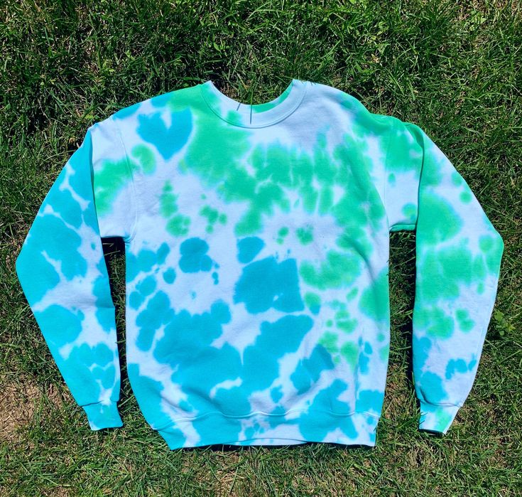 a blue and green tie - dyed sweatshirt laying on the grass