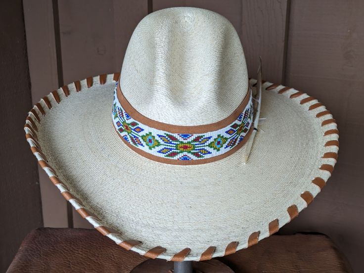 The Jasmine hat starts with a Gus fine palm hat body that is made in Mexico. It has a 4" brim and 5 1/2" crown. Hand laced in saddle color leather lace. The hatband has a layer of saddle tan suede that serves as the background for the beaded strip. The back of the band has 3 mini Conchos. Finished with a "red tail hawk" feather that is created from a turkey feather. Note: Hats are made to order. Allow up to 4 weeks for your hat to ship. Adjustable High Crown Hat Bands For Country Events, Artisan Hat Bands For Kentucky Derby, Country Style Festival Hat Bands With High Crown, Western Straw Hat With High Crown For Ranch, Artisan Straw Hat With Short Brim For Country Events, Traditional Brimmed Straw Hat For Rodeo, Traditional Hats With Curved Brim For Country Events, Traditional Curved Brim Hats For Country Events, Custom Adjustable Wide Brim Panama Hat