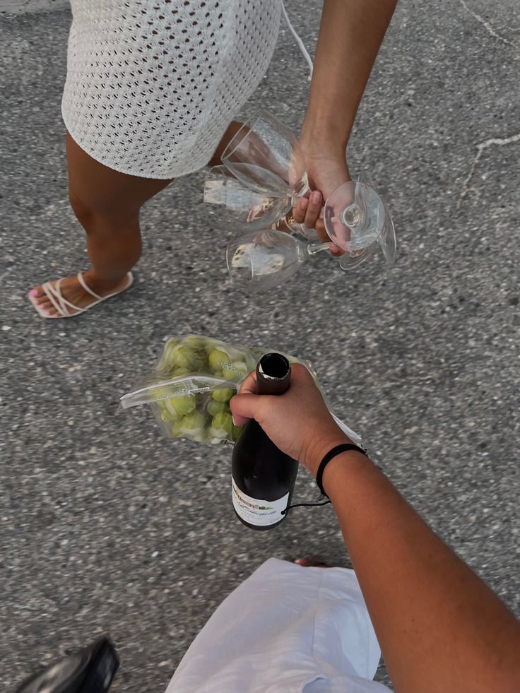 two people holding wine bottles and grapes in their hands while another person is sitting on the ground