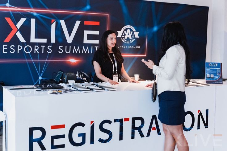 two women standing at a counter in front of a sign that says xlive esports summit