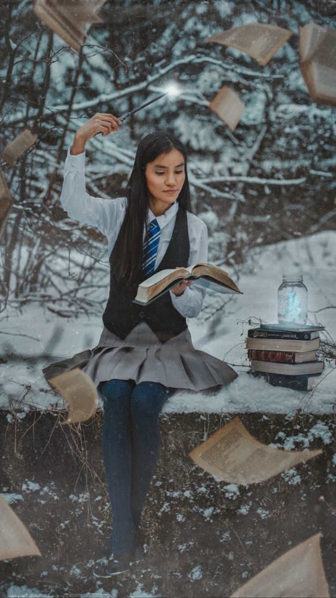 a woman sitting on top of a snow covered ground next to books flying in the air