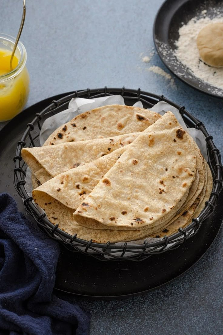 three tortillas in a black bowl on a plate next to some orange juice