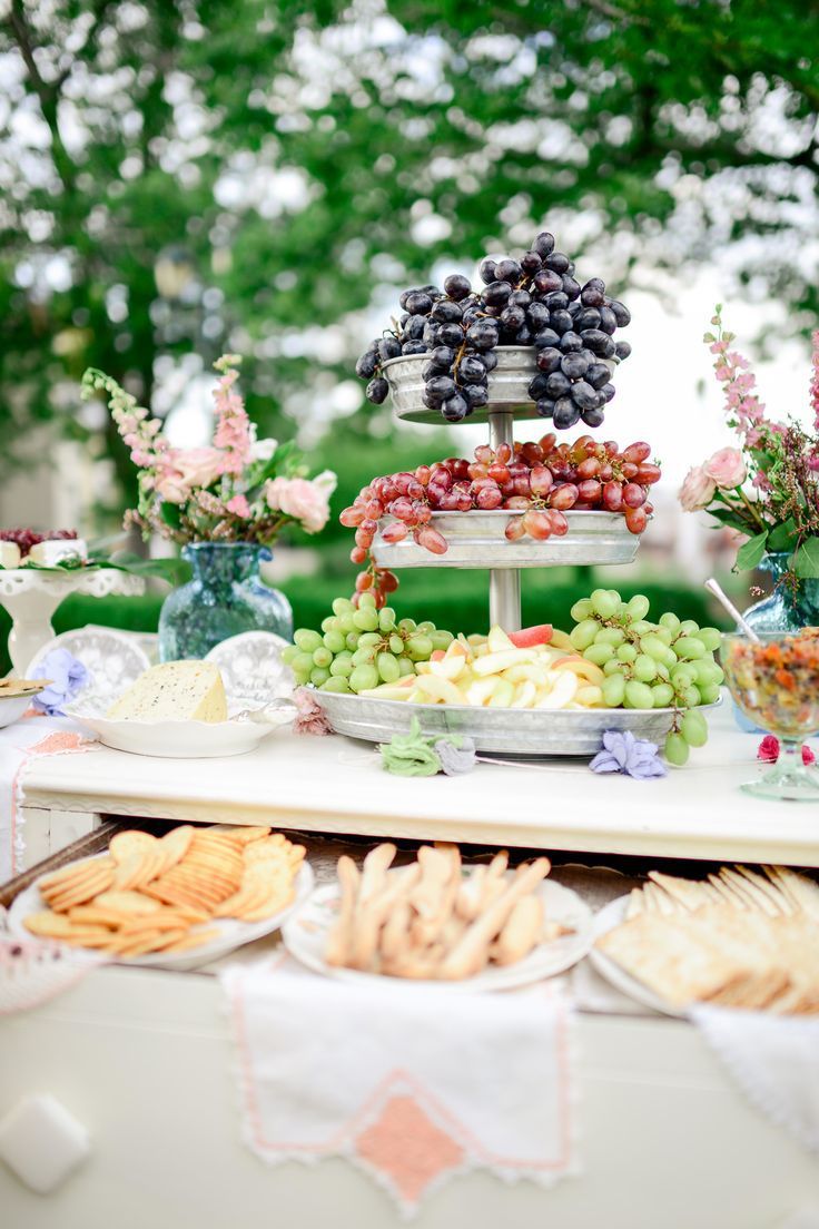 a table topped with grapes and crackers on top of a white table covered in flowers