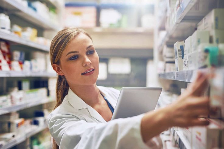 a female pharment is looking at the shelves in a pharmacy store and smiling