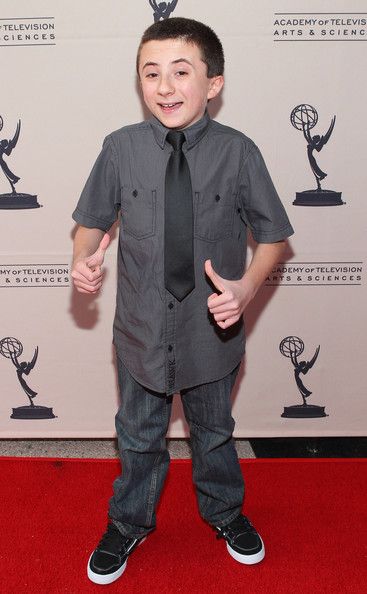 a young boy giving the thumbs up while standing on a red carpet