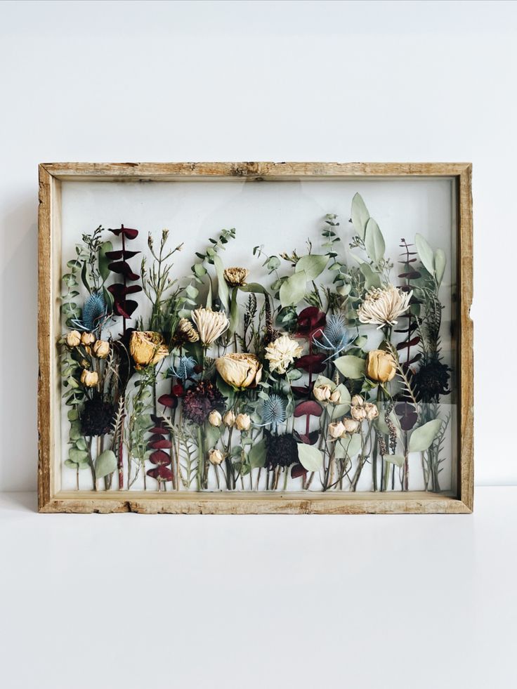 a wooden frame filled with flowers on top of a white wall