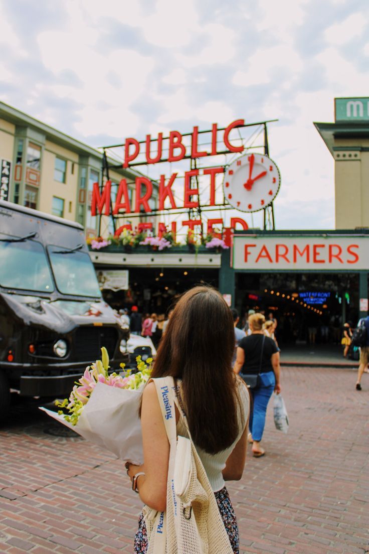 a woman holding flowers in front of a farmers market