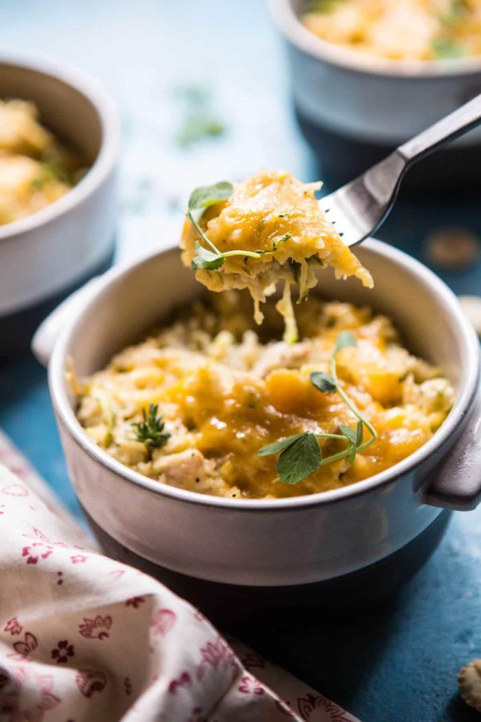 a spoon full of food is being lifted from a casserole dish with cheese and herbs