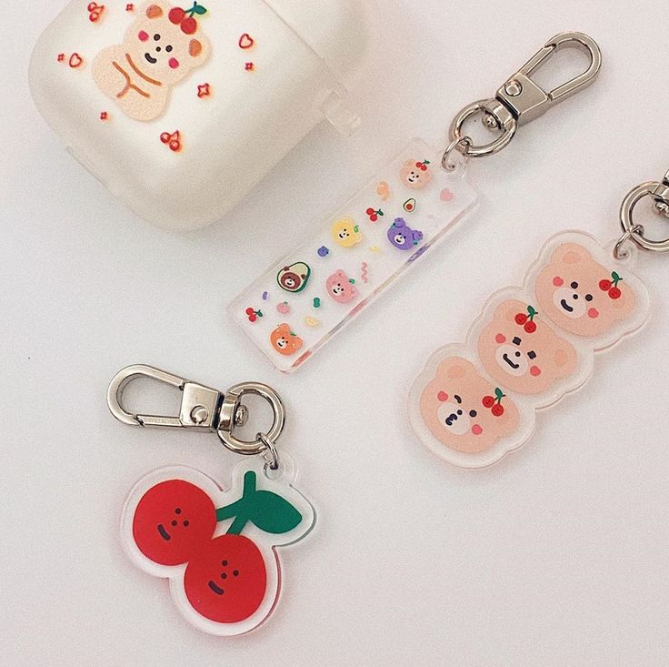 three keychains with different designs on them sitting next to an apple and strawberry