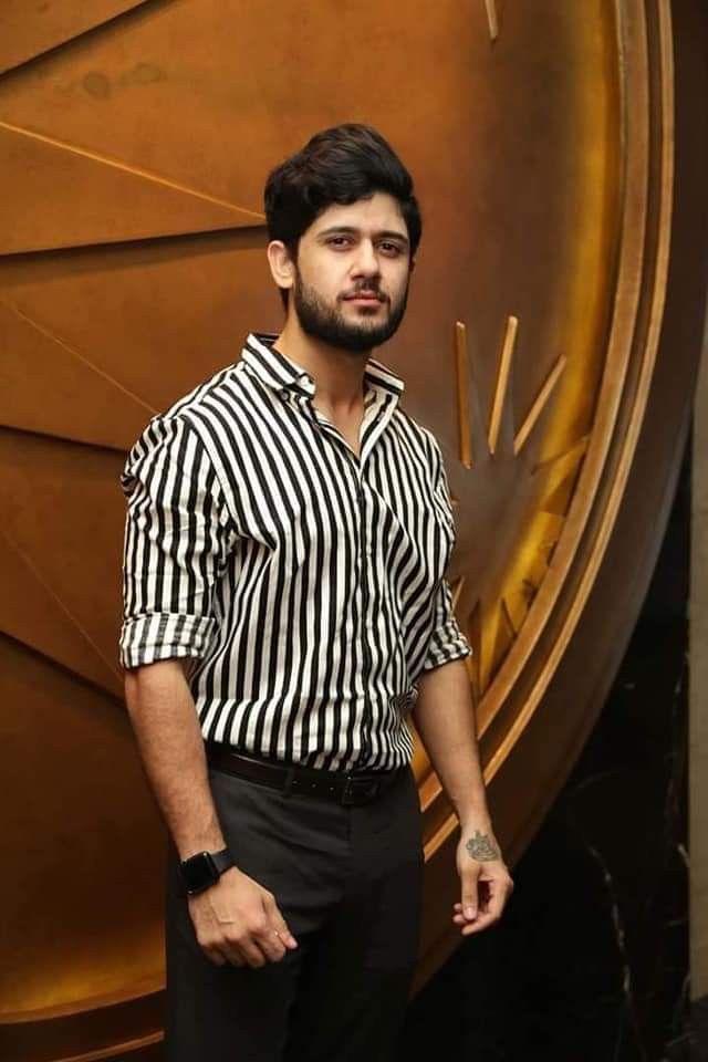 a man standing in front of a wall with a clock on it's face