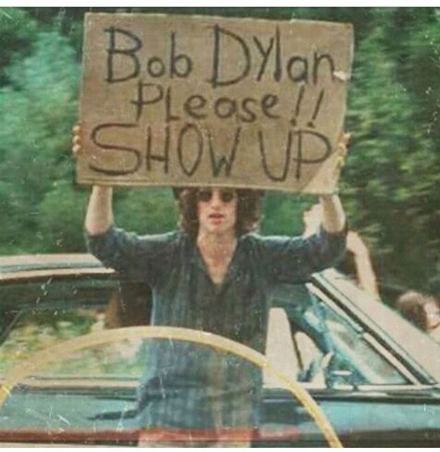 a man holding up a sign that says bob dylan please show up