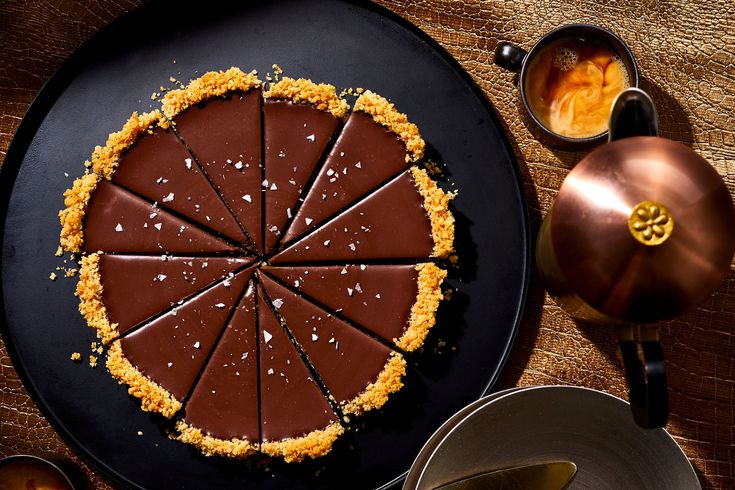 a chocolate tart on a black plate next to tea pots and silver wares