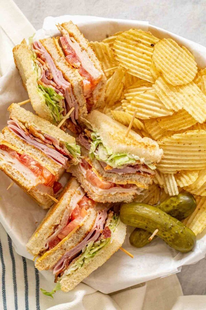 a white plate topped with a cut in half sandwich next to chips and pickles