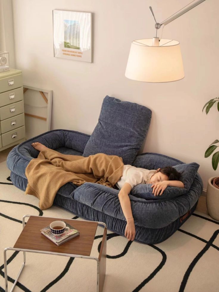 a woman laying on top of a blue couch in a living room next to a lamp