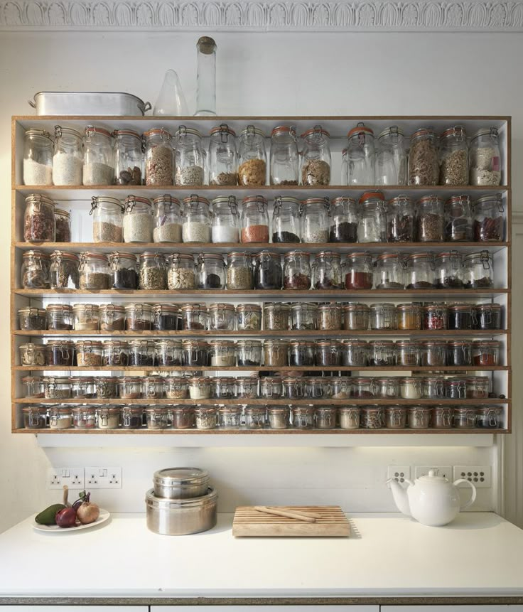 a shelf filled with lots of jars on top of a white counter next to a pot and pan