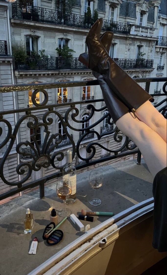 a woman's legs with high heels on top of a balcony overlooking the city