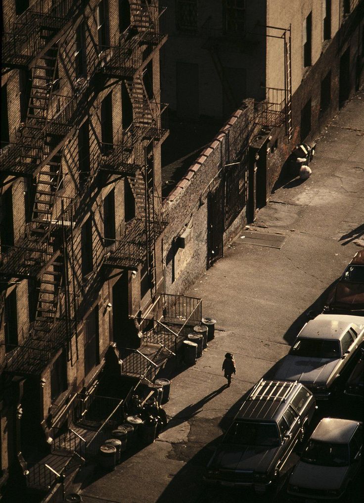 an aerial view of a man walking down the street in front of some buildings with fire escapes