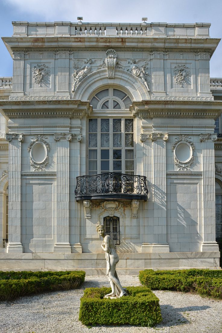 a large white building with a statue in front of it and bushes around the perimeter