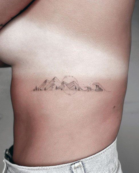 a woman's stomach has a small mountain tattoo on her left side ribcage