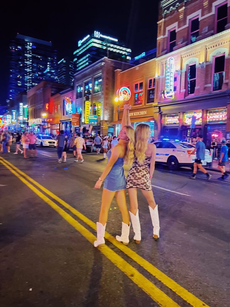 two women are dancing in the middle of the street while people walk by at night