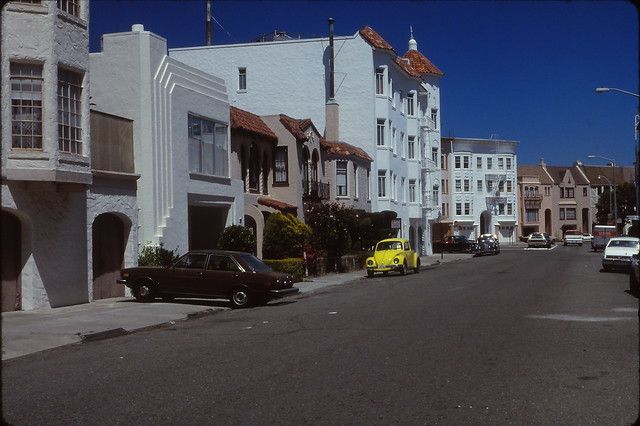 cars are parked on the street in front of white buildings